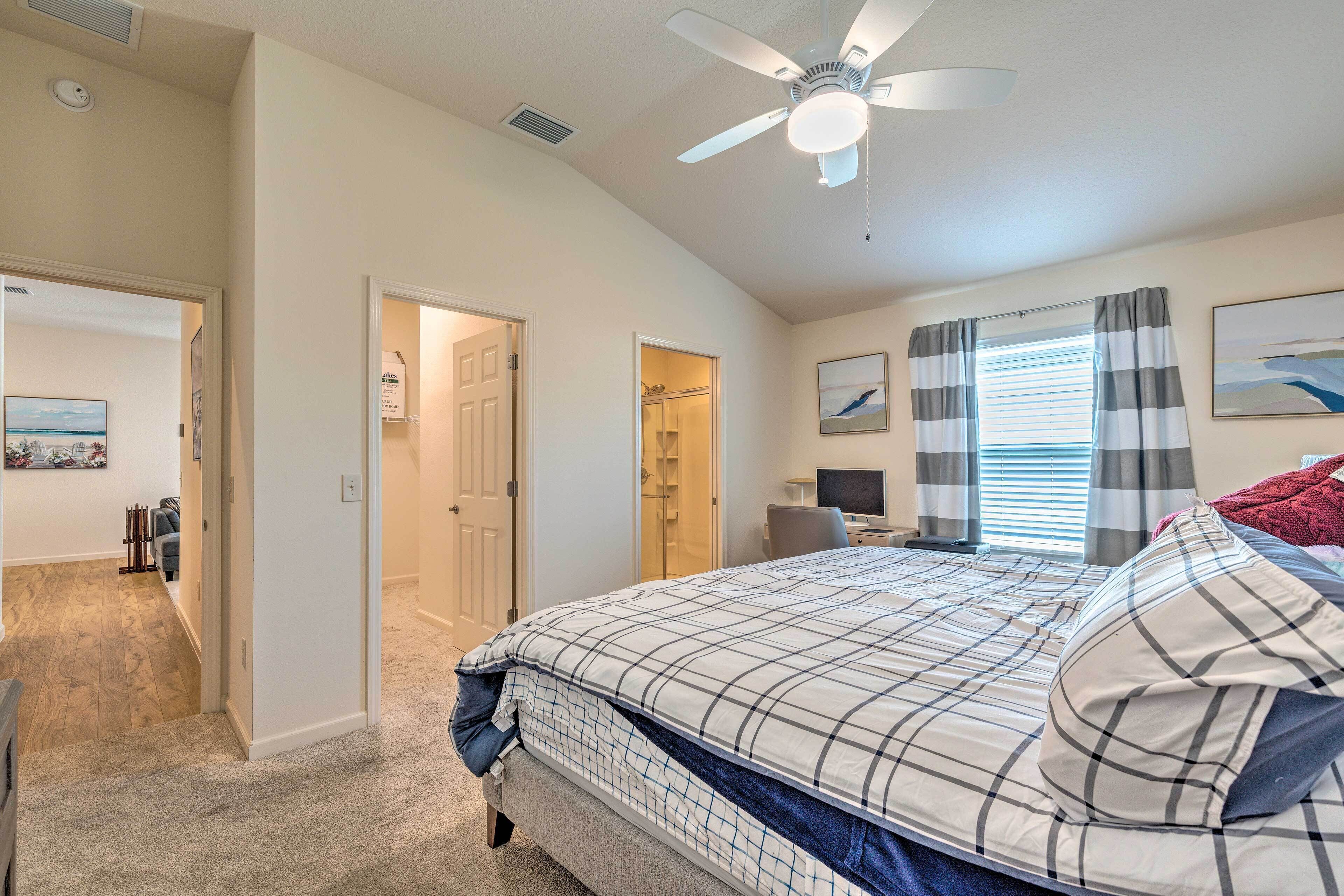 A bedroom with a bed, a ceiling fan, a desk with a computer, and a window with curtains.