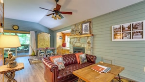 A cozy living room with a leather sofa, wooden coffee table, and a stone fireplace. - Cozy Creekside Cabin w/ Fire Pit & Views! (Hayesville)