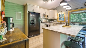 A kitchen with a large island, white cabinets, a stainless steel refrigerator, a microwave, and a stove. - Cozy Creekside Cabin w/ Fire Pit & Views! (Hayesville)