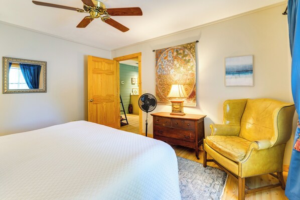 A bedroom with a bed, a wooden chair, a nightstand, a fan, and a ceiling fan.
