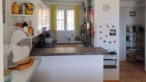 Cuina amb armaris blancs, un ventilador, un rentaplat i una finestra amb cortines grogues.