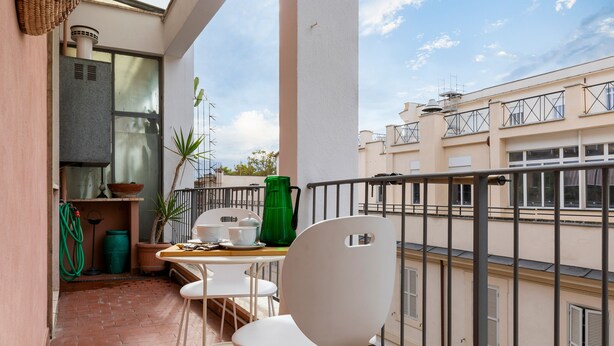 Ein Balkon mit Tisch, Stühlen, einer grünen Vase und einem Topfpflanzen.