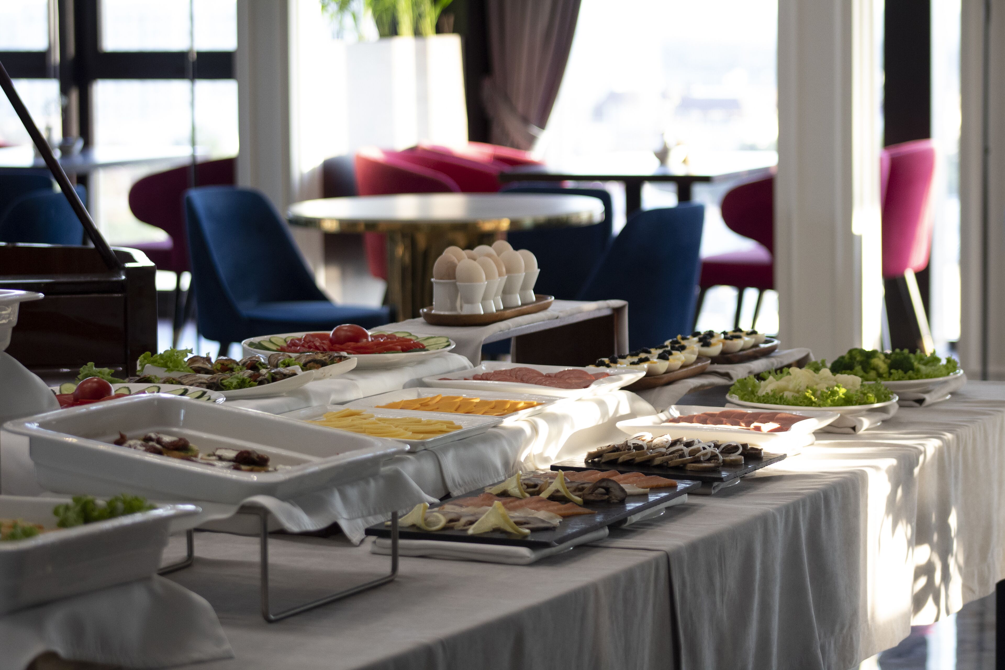 A buffet table with various food items and a seating area with chairs and tables in the background.