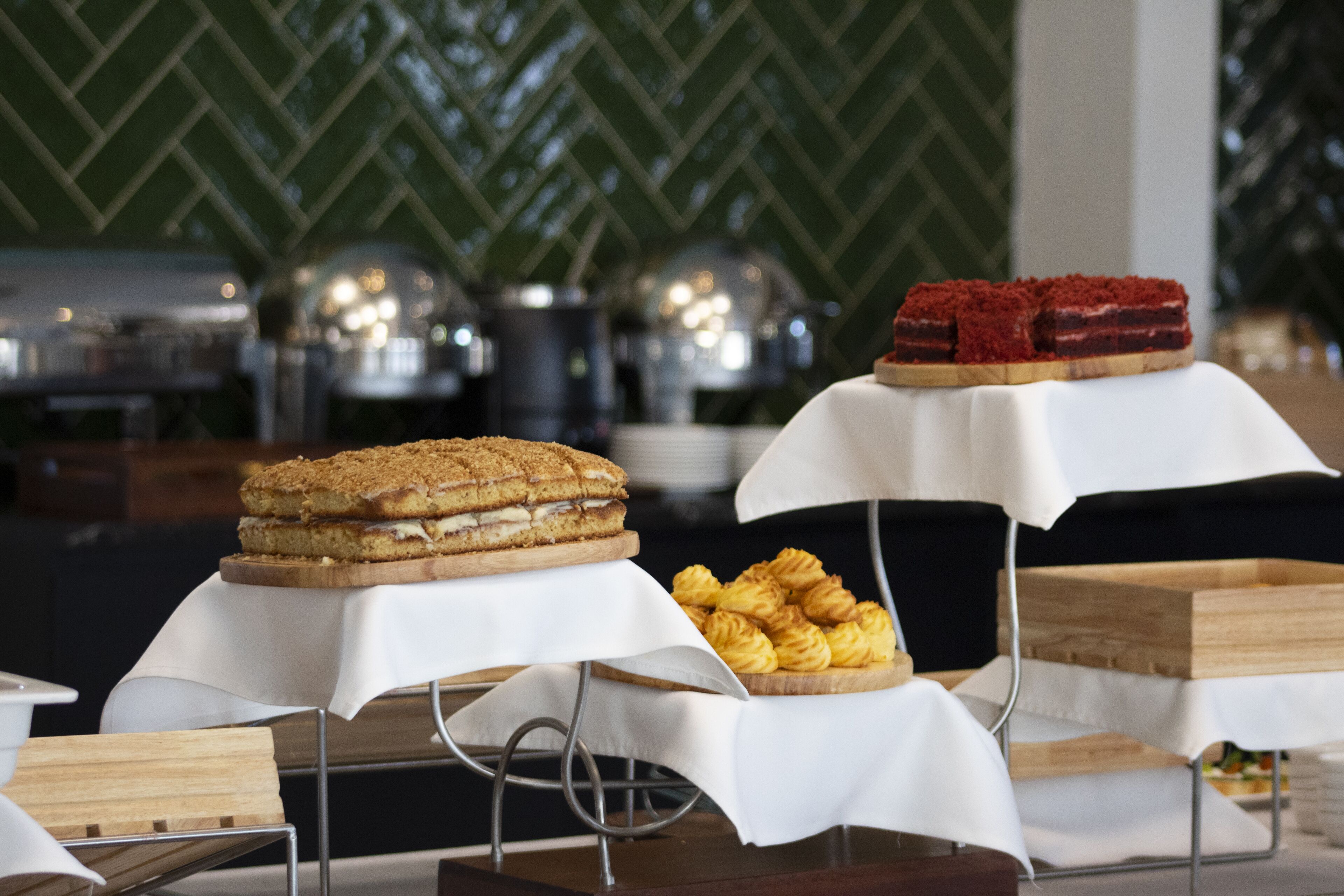 Une table de buffet proposant divers desserts et pâtisseries, dont un gâteau à plusieurs couches et des choux à la crème, le tout disposé devant un mur à motifs verts.