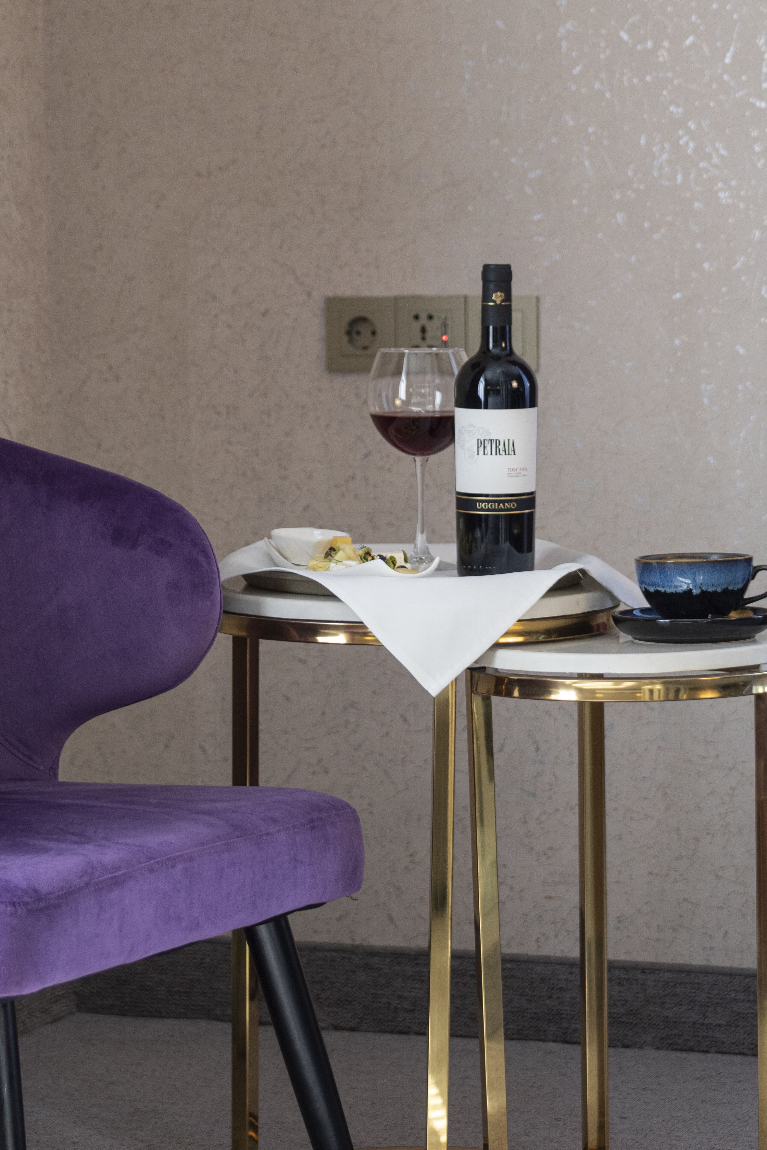 A purple chair, a table with a wine bottle, a glass of wine, and a bowl on a small round table.