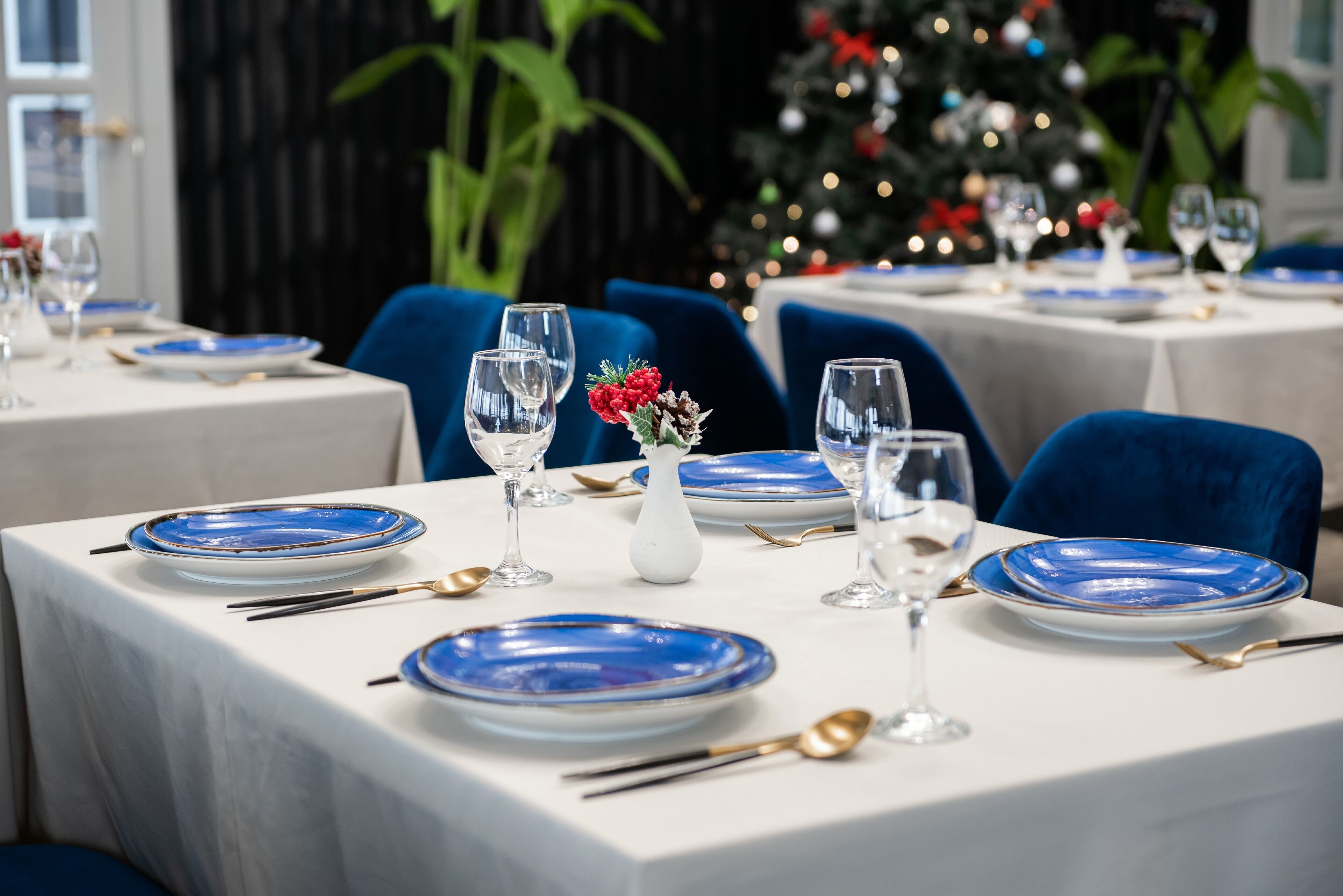 A dining area with tables set for two, featuring blue plates and white tablecloths.