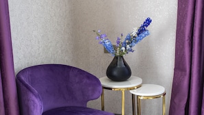 A purple chair, a small round table with a vase of flowers, and a curtain in a corner. - Orient Hotel Bishkek (Bishkek)