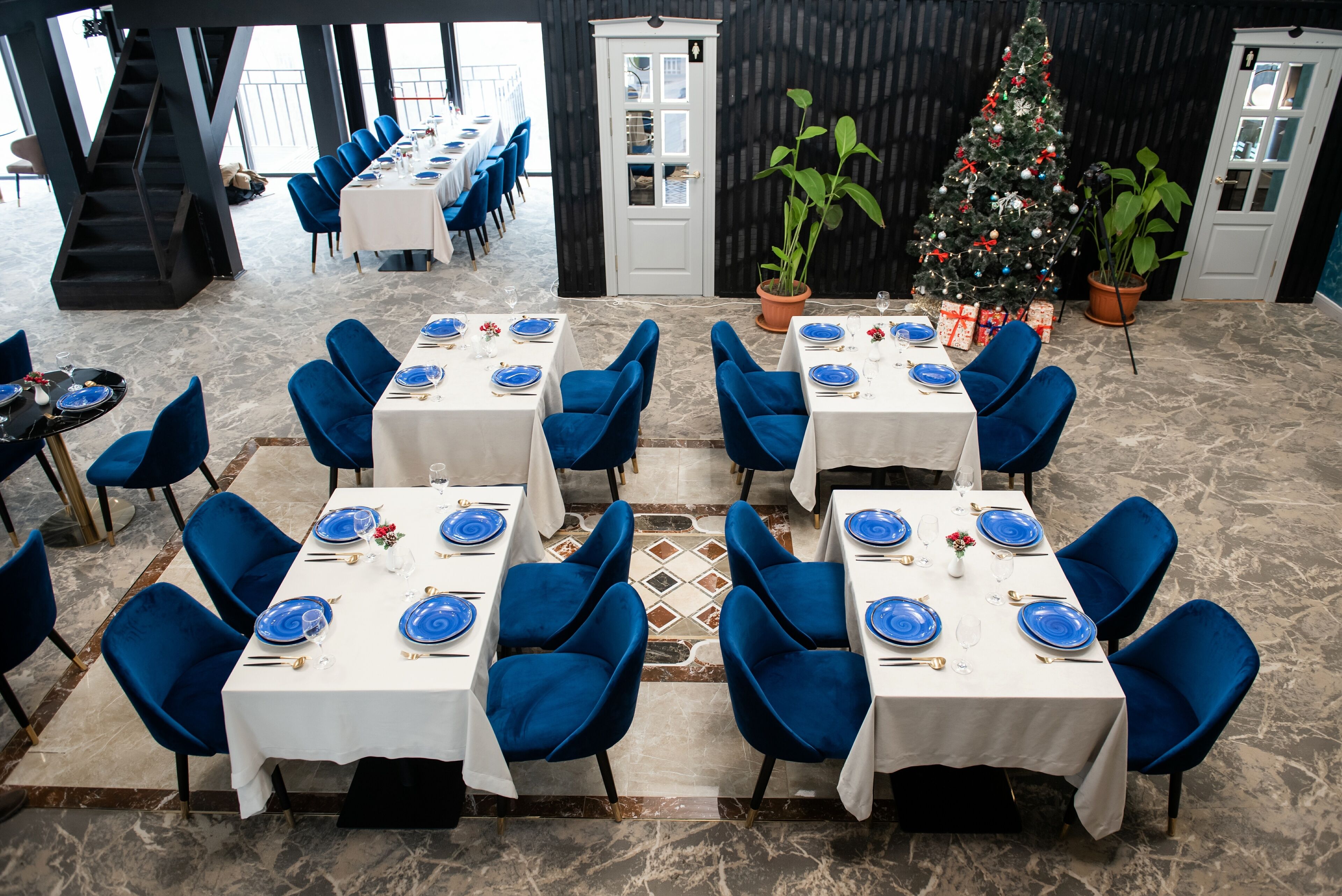 Un coin repas avec des tables dressées pour quatre personnes, des chaises bleues et un sapin de Noël.