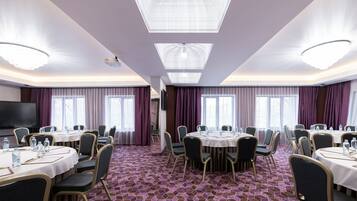 Ein Konferenzraum mit mehreren Tischen, Stühlen und einer großen Leinwand.