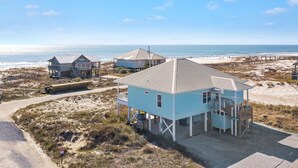 A coastal property with multiple buildings, including a prominent light blue house with a balcony, situated on sandy terrain with a beach and ocean in the background. - Gorgeous 3 Bd/ 2+Ba home w/unobstructed views & easy beach access (Gulf Shores)