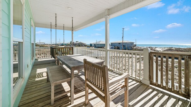 A wooden deck with a table and chairs, overlooking a beach with buildings in the background. - Gorgeous 3 Bd/ 2+Ba home w/unobstructed views & easy beach access (Gulf Shores)
