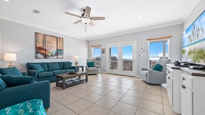 A spacious living room with teal sofas, a coffee table, and a ceiling fan. - Gorgeous 3 Bd/ 2+Ba home w/unobstructed views & easy beach access (Gulf Shores)