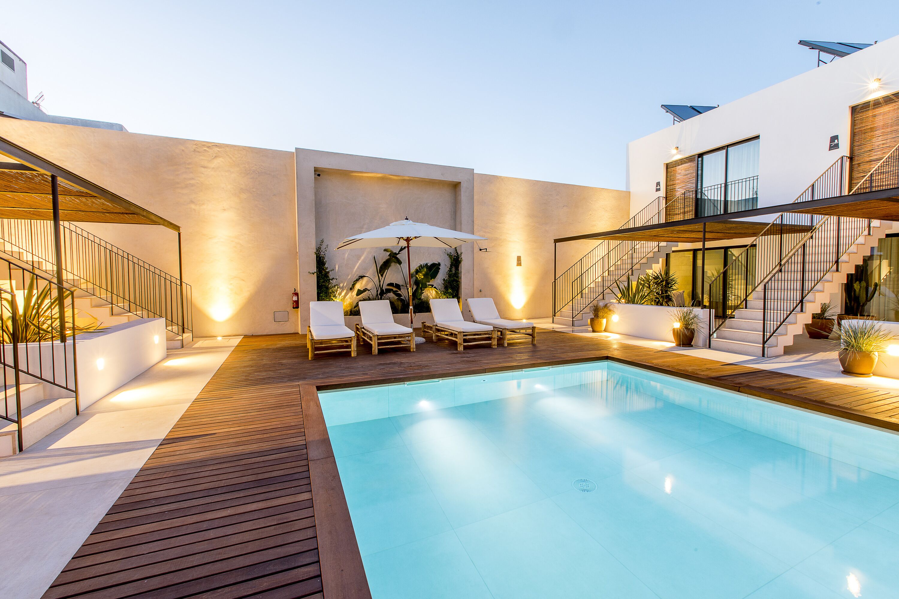 A modern outdoor pool area with a wooden deck, lounge chairs, and a staircase leading to an upper level.