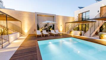 A modern outdoor pool area with a wooden deck, lounge chairs, and a staircase leading to an upper level.