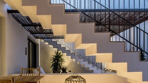Una escalera moderna con patrones geométricos, una mesa de madera con sillas e iluminación decorativa.