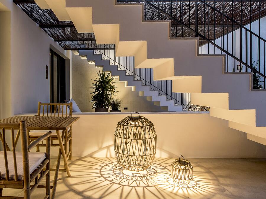 A modern staircase with geometric patterns, a wooden table with chairs, and decorative lighting.