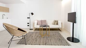 Een moderne woonkamer met een bank, een rond bijzettafeltje, een rieten fauteuil, een vloerlamp en een tv op een dressoir.