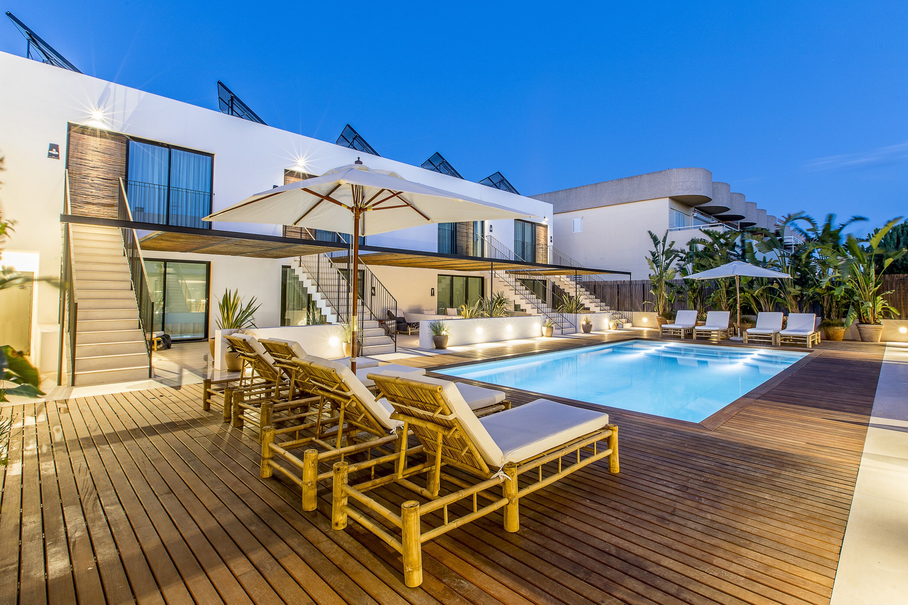Un área de piscina moderna al aire libre con terraza de madera, sillas de descanso y sombrillas.