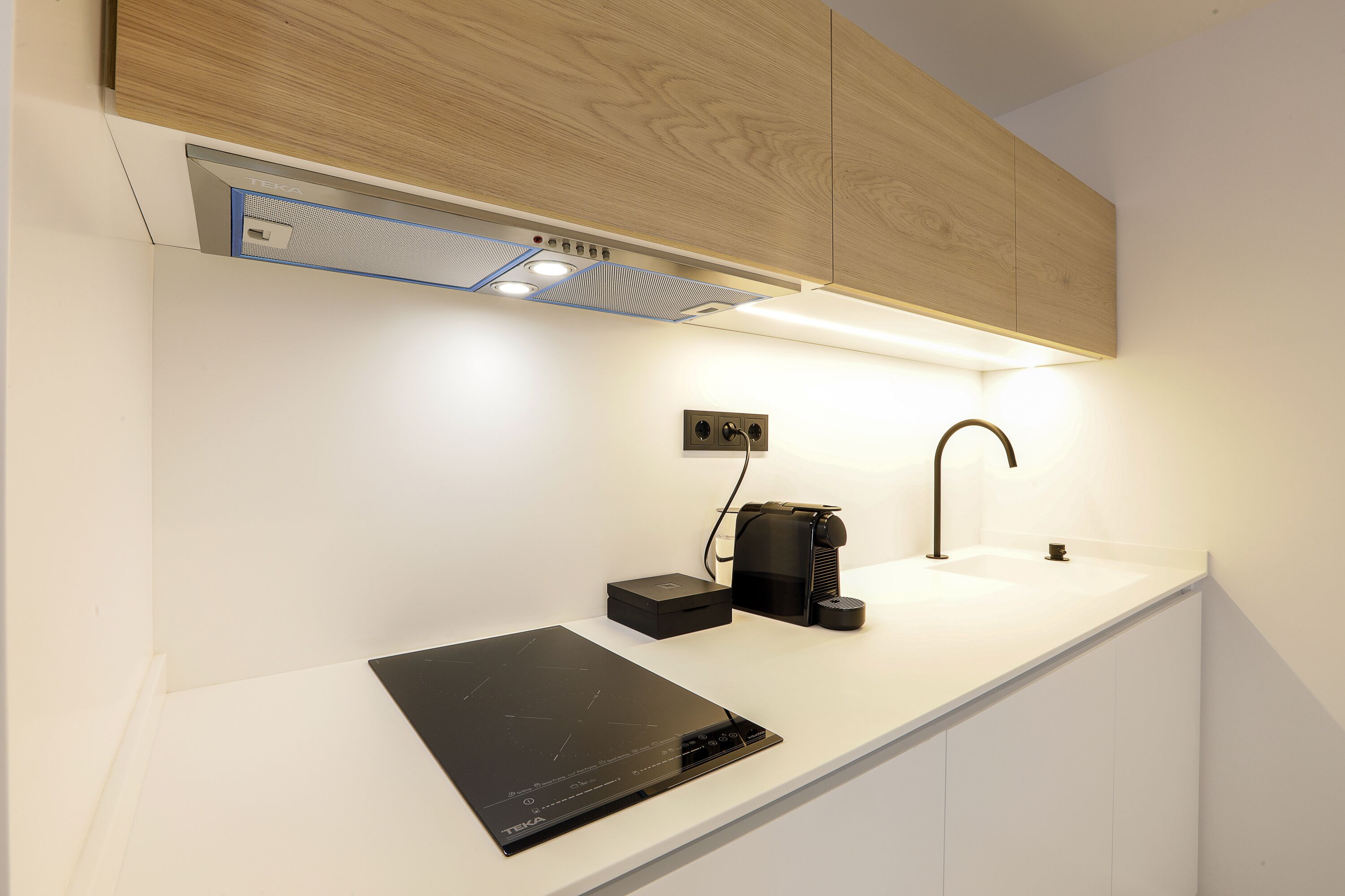 Una cocina moderna con una placa de inducción integrada, una cafetera y un lavabo.