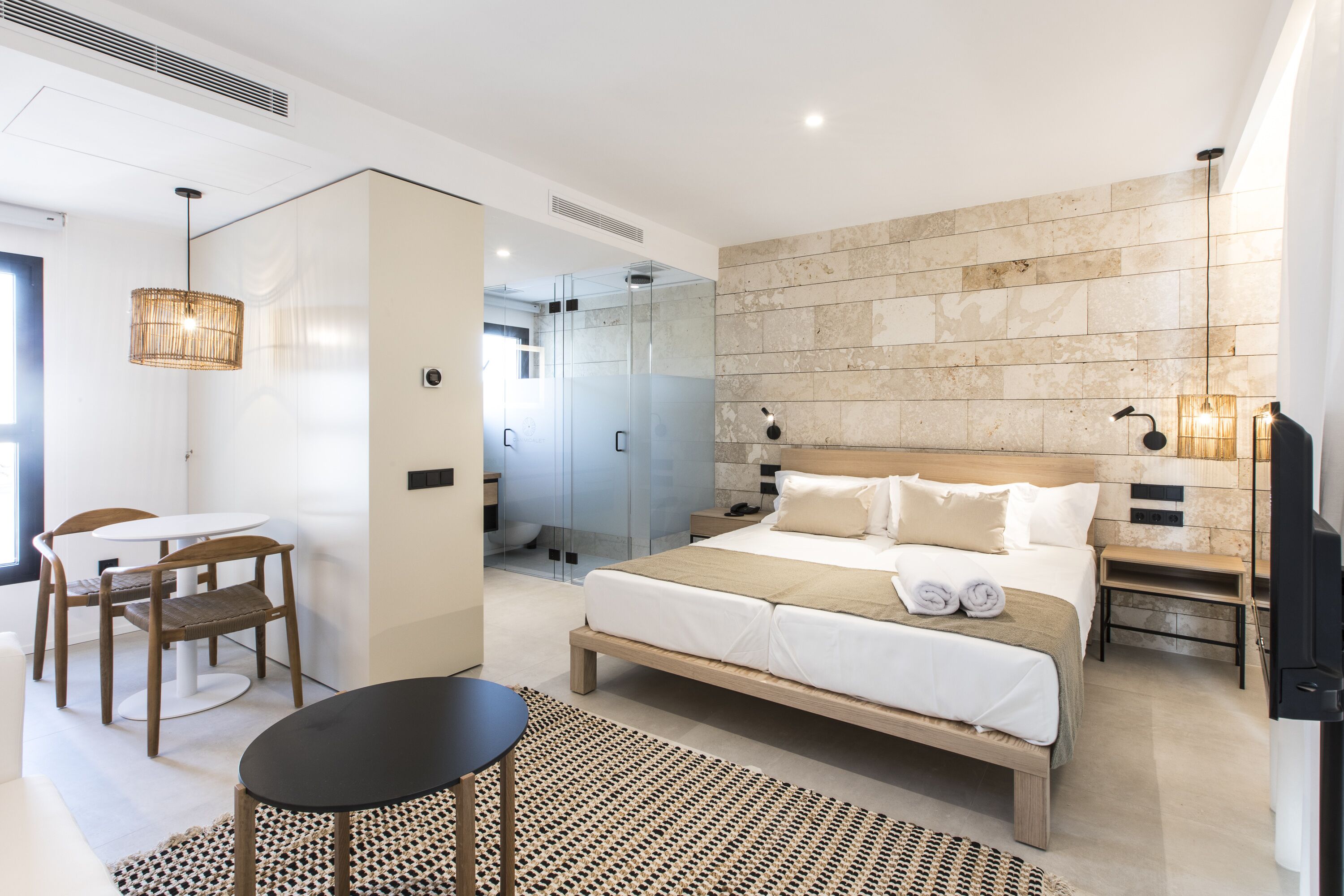 Una habitación de hotel moderna con una cama grande, una zona de estar con una mesa y sillas, un escritorio pequeño y un baño con cabina de ducha de vidrio.