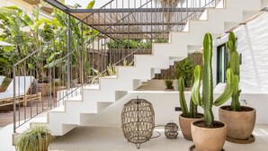 Una escalera moderna con paredes blancas y barandillas metálicas, rodeada de plantas en macetas, incluyendo cactus y una cesta colgante.