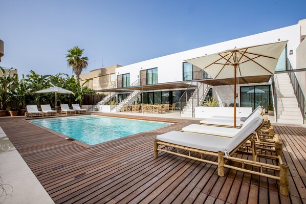 A modern outdoor pool area with wooden decking, lounge chairs, and umbrellas. - Can Micalet Formentera (Formentera)