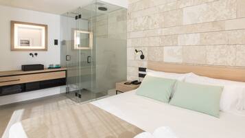 A modern hotel room with a glass-enclosed shower, a wooden headboard, and a large bed with green pillows.