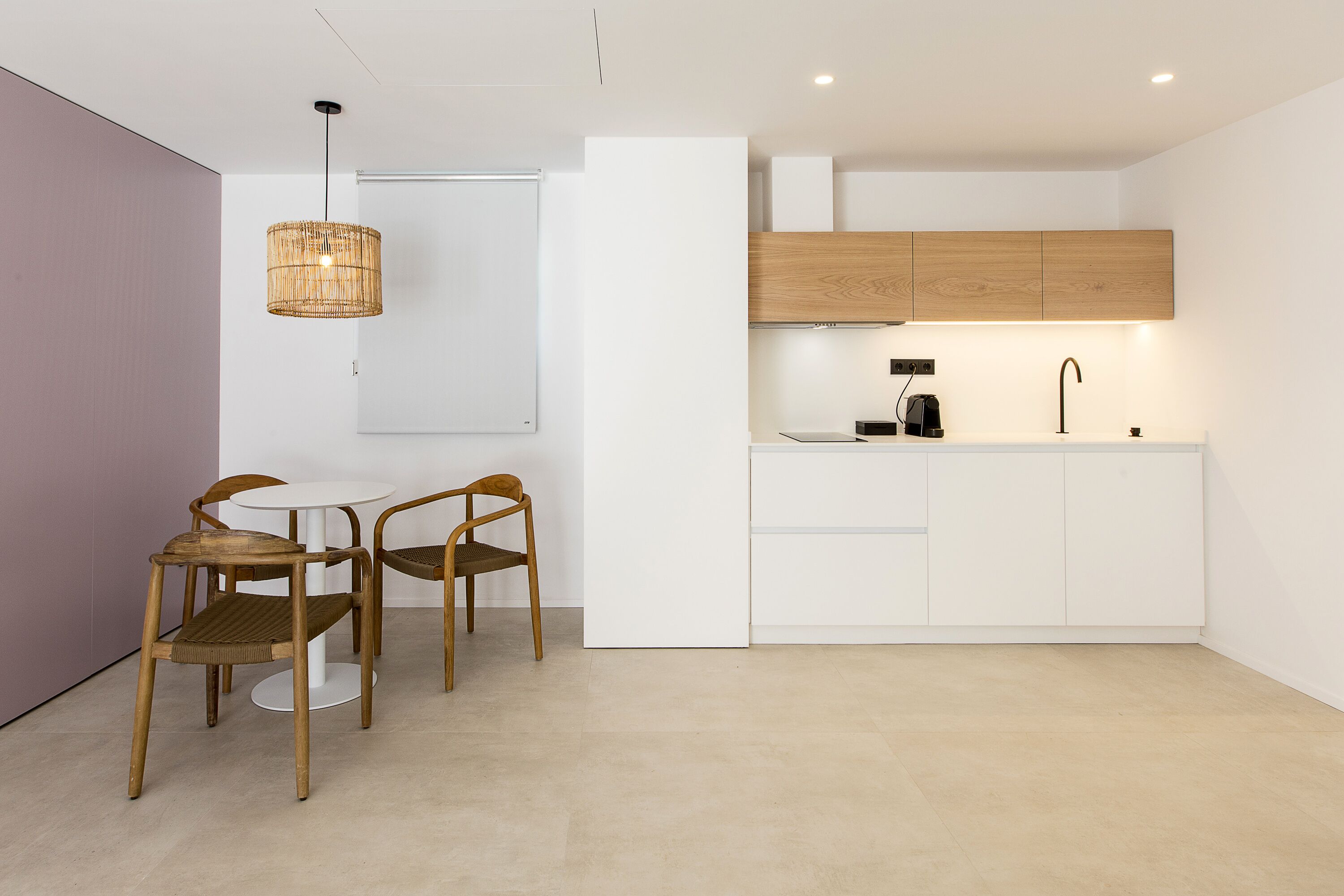 Una cocina moderna con armarios blancos, encimera de madera y una lámpara colgante.