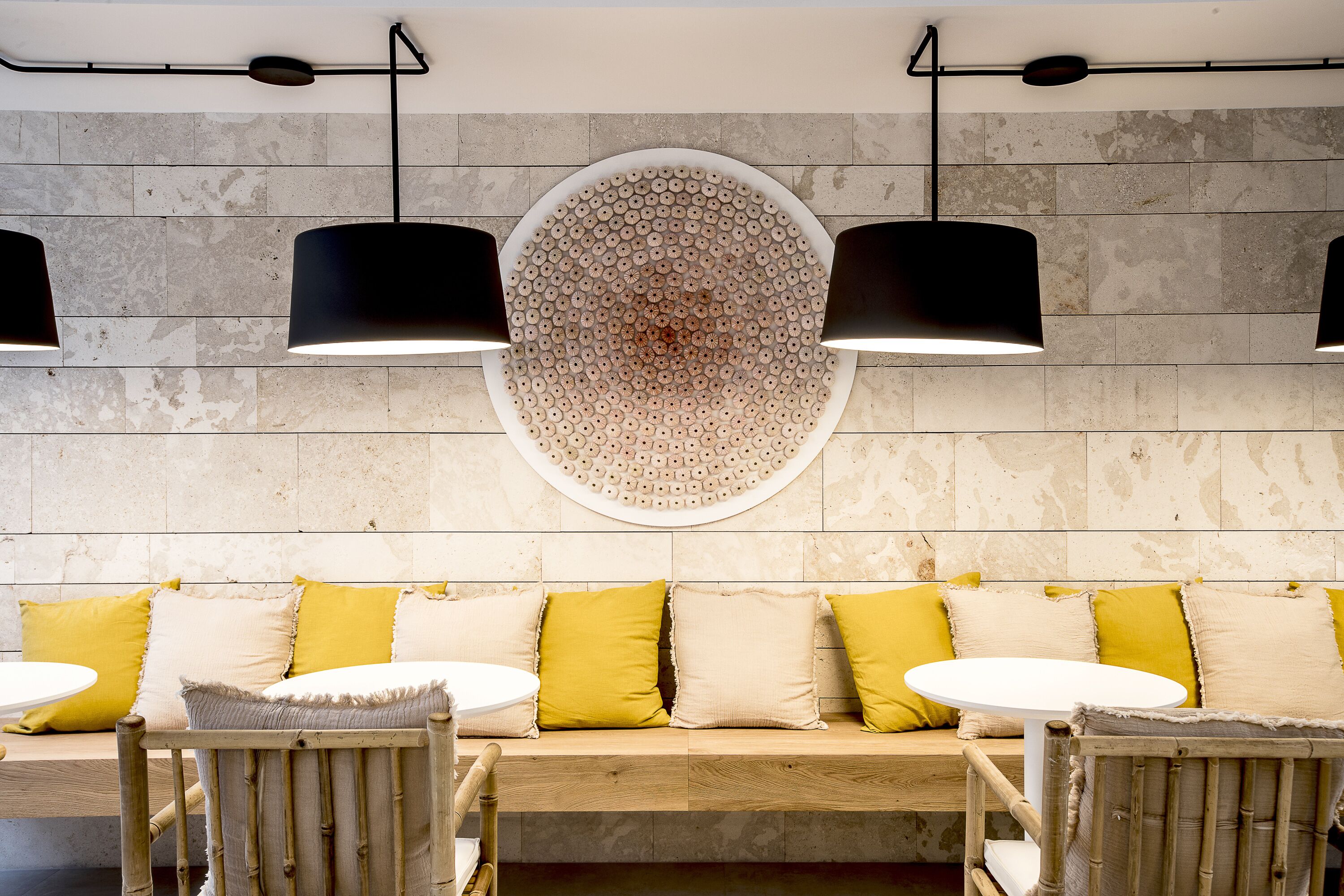 A seating area with a round wall decoration, two pendant lights, and a wooden bench with yellow cushions.