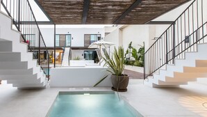Un área de piscina interior moderna con una piscina central, rodeada de paredes blancas y un techo de madera.