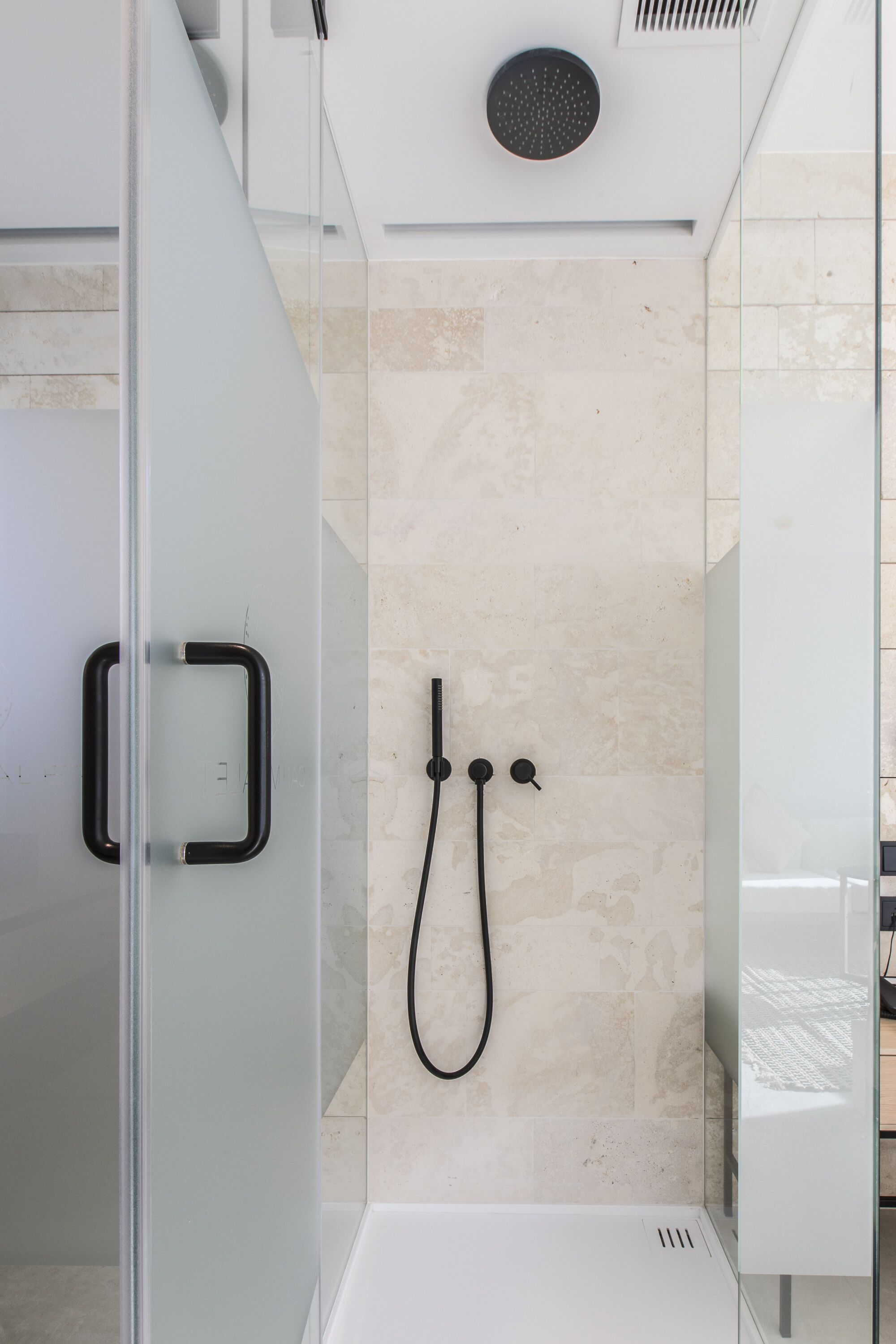 Una ducha moderna con cabina de vidrio, cabezal de ducha manual y panel de control empotrado.