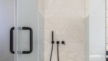 Una ducha moderna con cabina de vidrio, cabezal de ducha manual y panel de control empotrado.