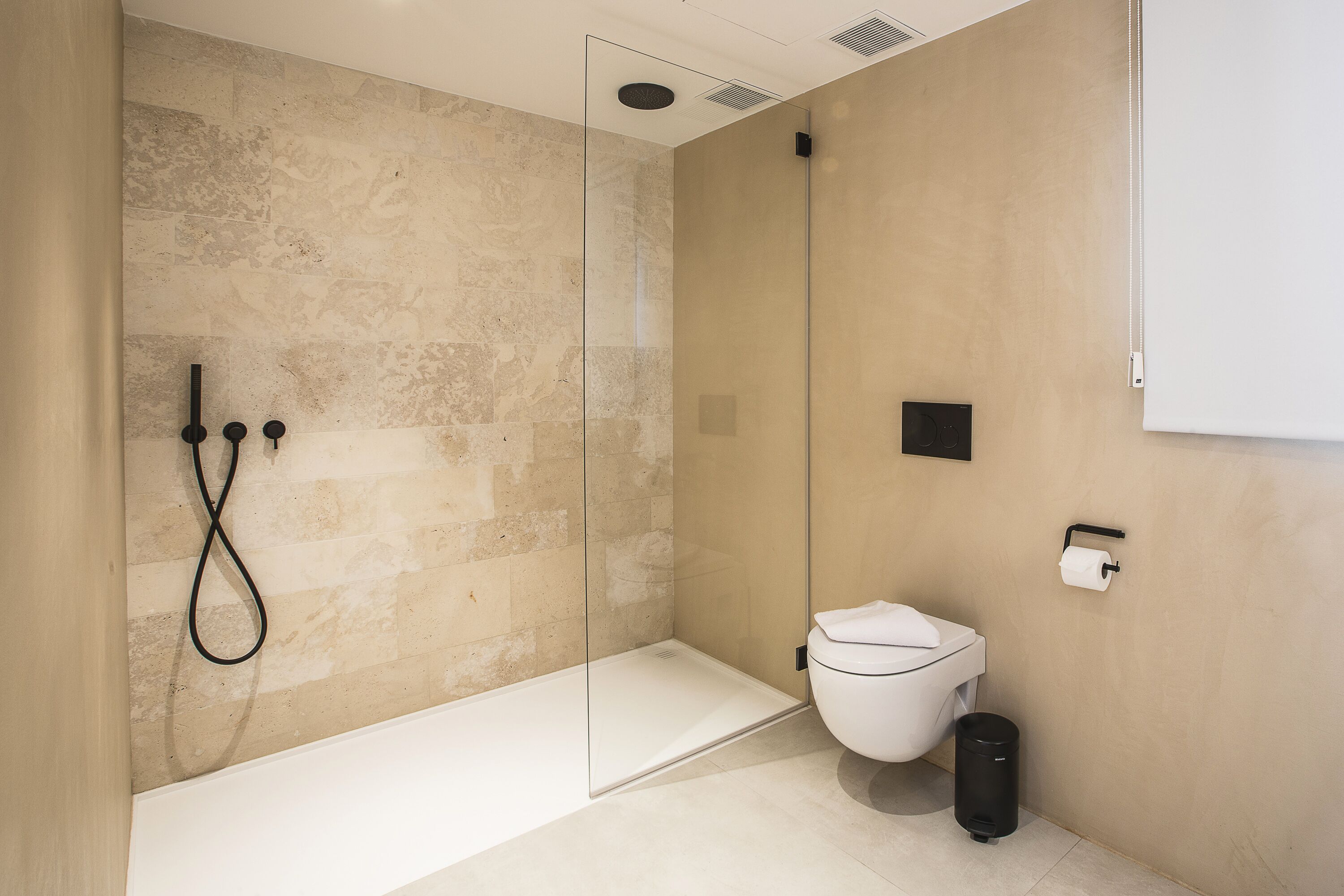 Un baño moderno con ducha envuelta en vidrio, inodoro blanco y cubo de basura negro.