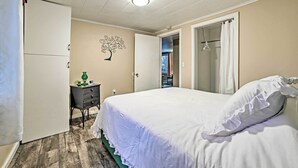 Une chambre à coucher comprenant un lit, une commode, une table de chevet, un élément décoratif mural et une porte donnant sur une autre pièce.