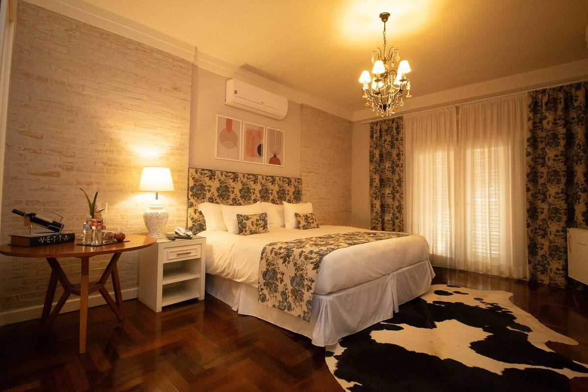 A bedroom with a bed, a chandelier, a wooden table, and a cowhide rug.