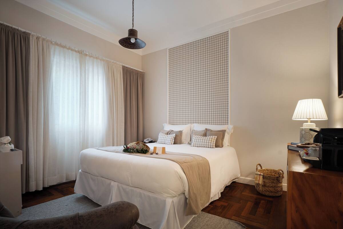 A hotel room with a large bed, a bedside table with a lamp, a chair, and a wooden floor.