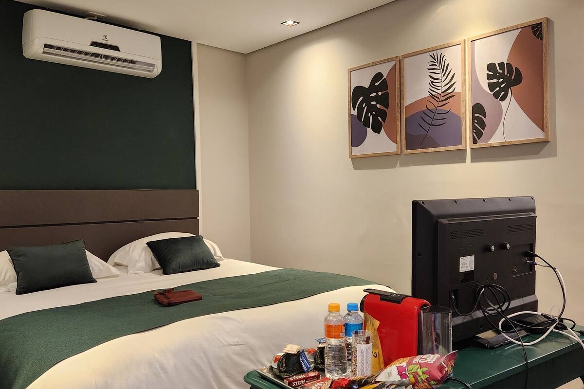A hotel room with a bed, a desk with a computer, and artwork on the wall.