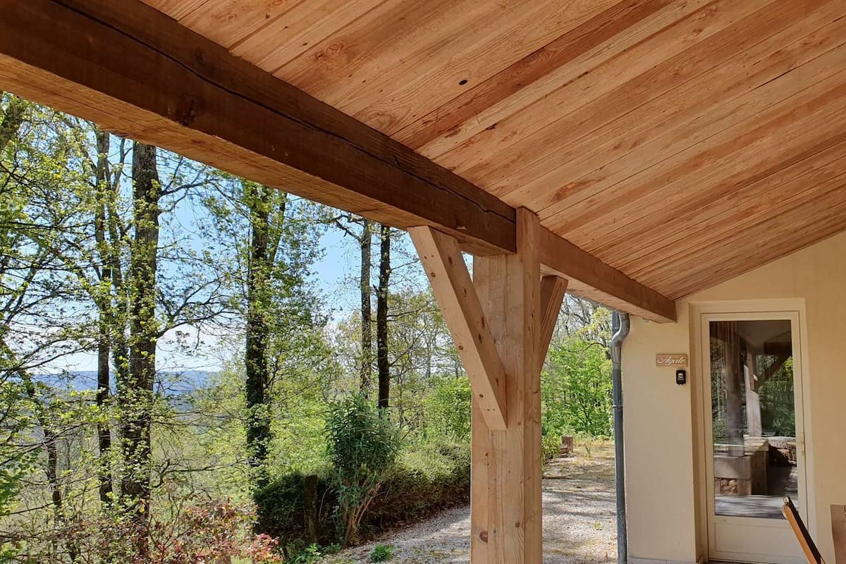A wooden pergola structure with a view of a forested area and a distant landscape.