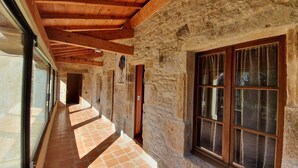 A corridor with stone walls, wooden beams, and large windows with curtains. - Domaine du Cardou (Puy-l'Eveque)