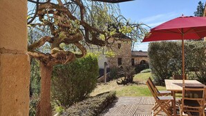A patio area with a table and chairs, a red umbrella, and a stone building in the background. - Domaine du Cardou (Puy-l'Eveque)