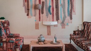 En stue med moderne abstrakt vægkunst, en stribet sofa, et lille bord med dekorative genstande og en hvid vægmonteret hylde.