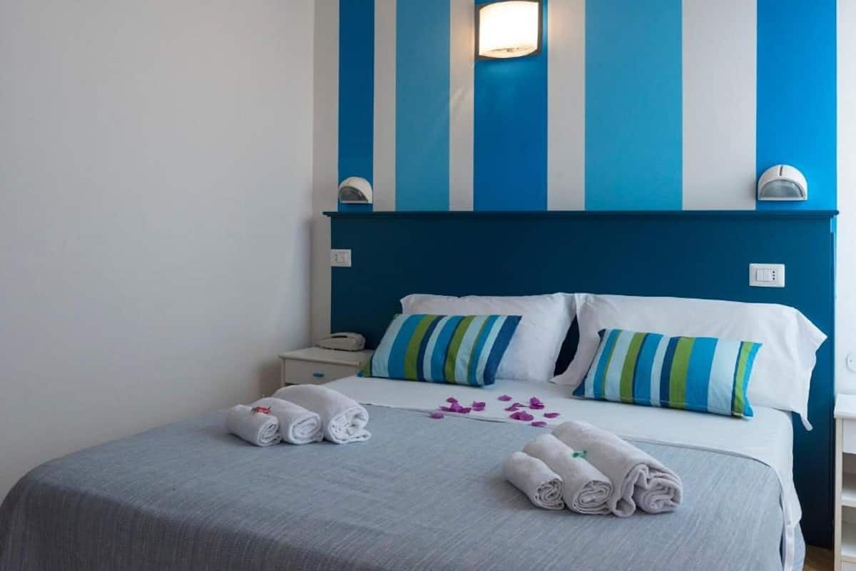 A hotel room with a bed, pillows, a nightstand, and a wall-mounted light fixture.