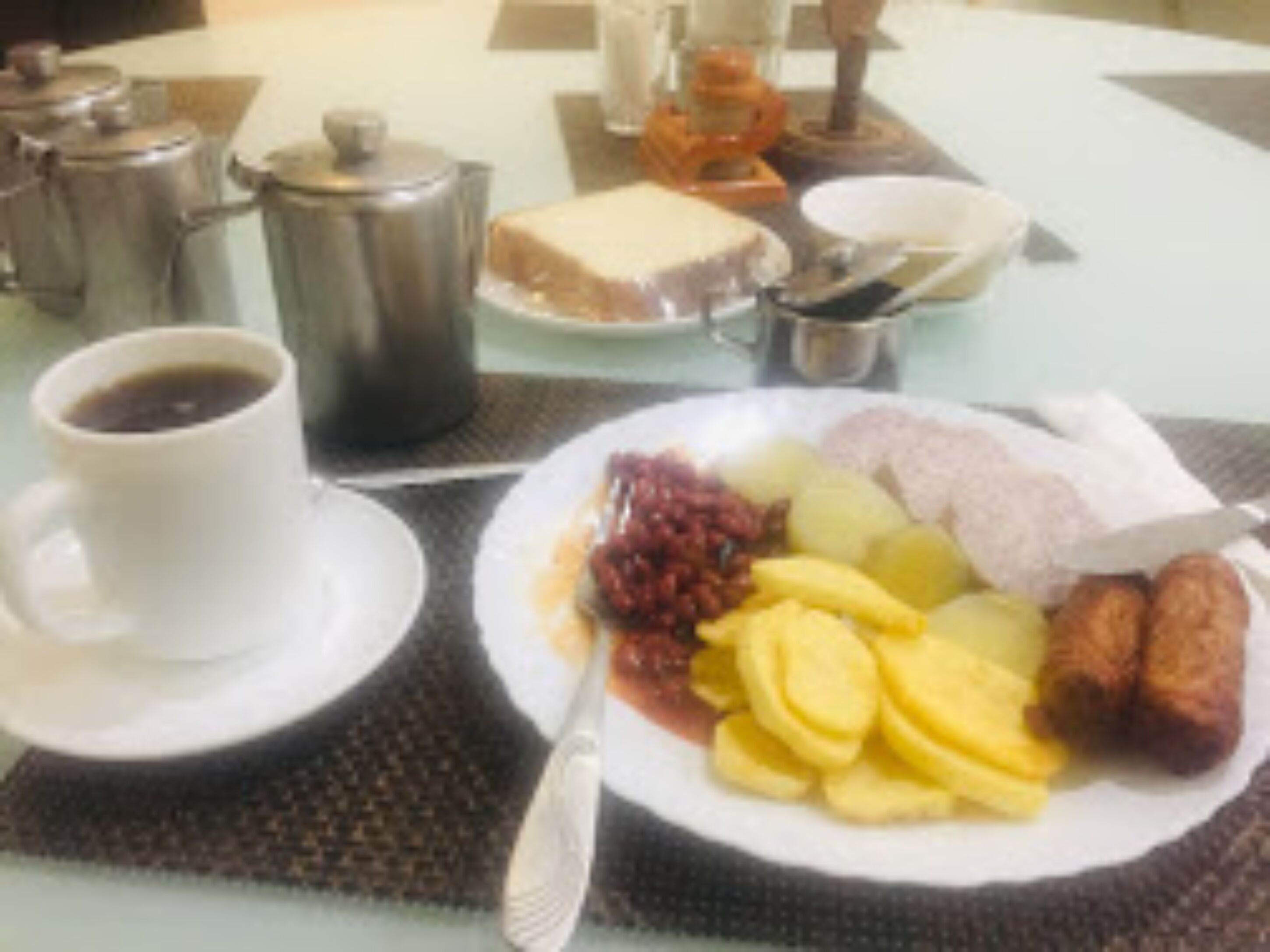 A breakfast table with a plate of sliced fruits, a cup of coffee, and a small bowl of jam.
