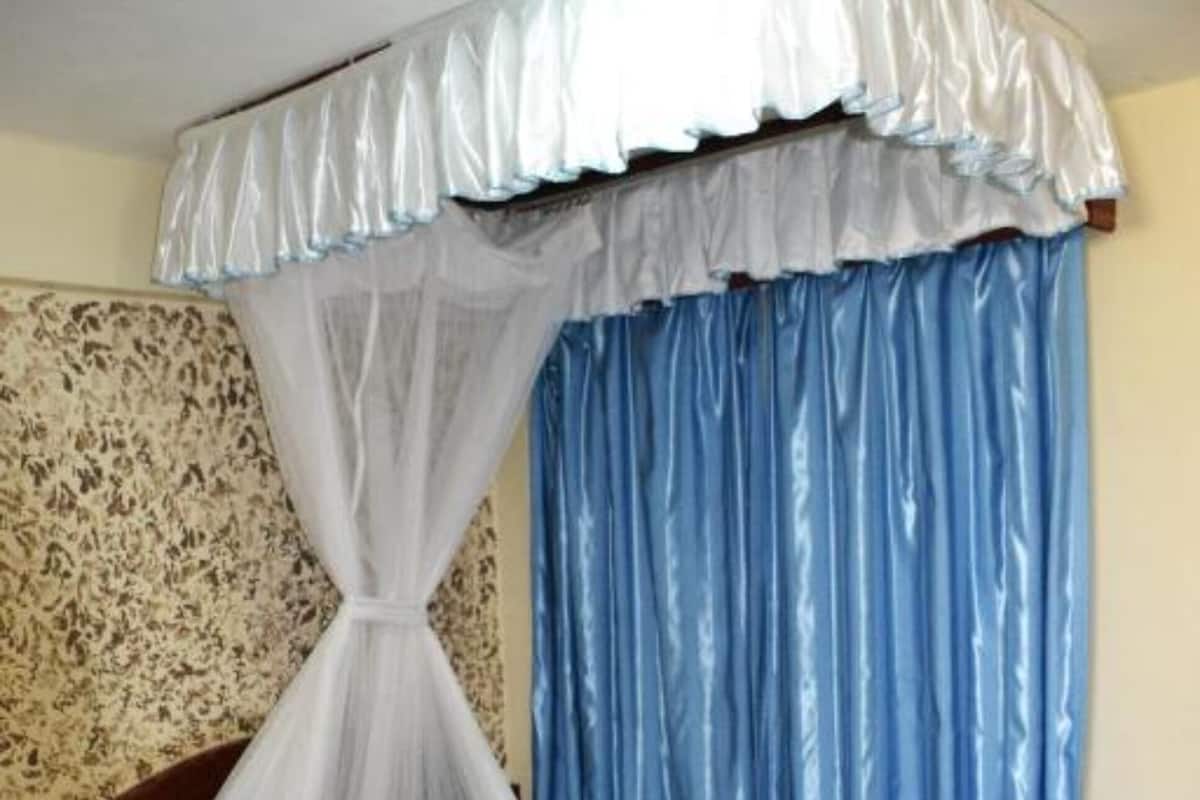 A bed with a canopy, striped bedding, and a headboard against a patterned wall.
