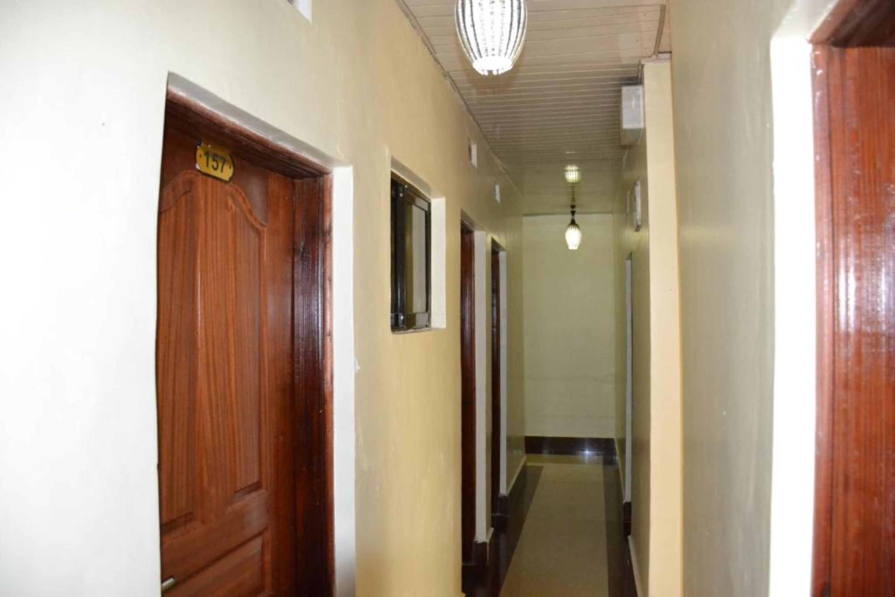 A hallway with wooden doors, a light fixture, and a number sign on the wall.