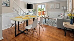 A spacious living area with a dining table, chairs, a sofa, and a balcony with a railing. - Asbury: Work Friendly & 40 Mins to DC (Sterling)