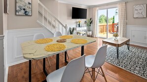 A dining area with a marble table, white chairs, and a view of the outdoors through a sliding glass door. - Asbury: Work Friendly & 40 Mins to DC (Sterling)