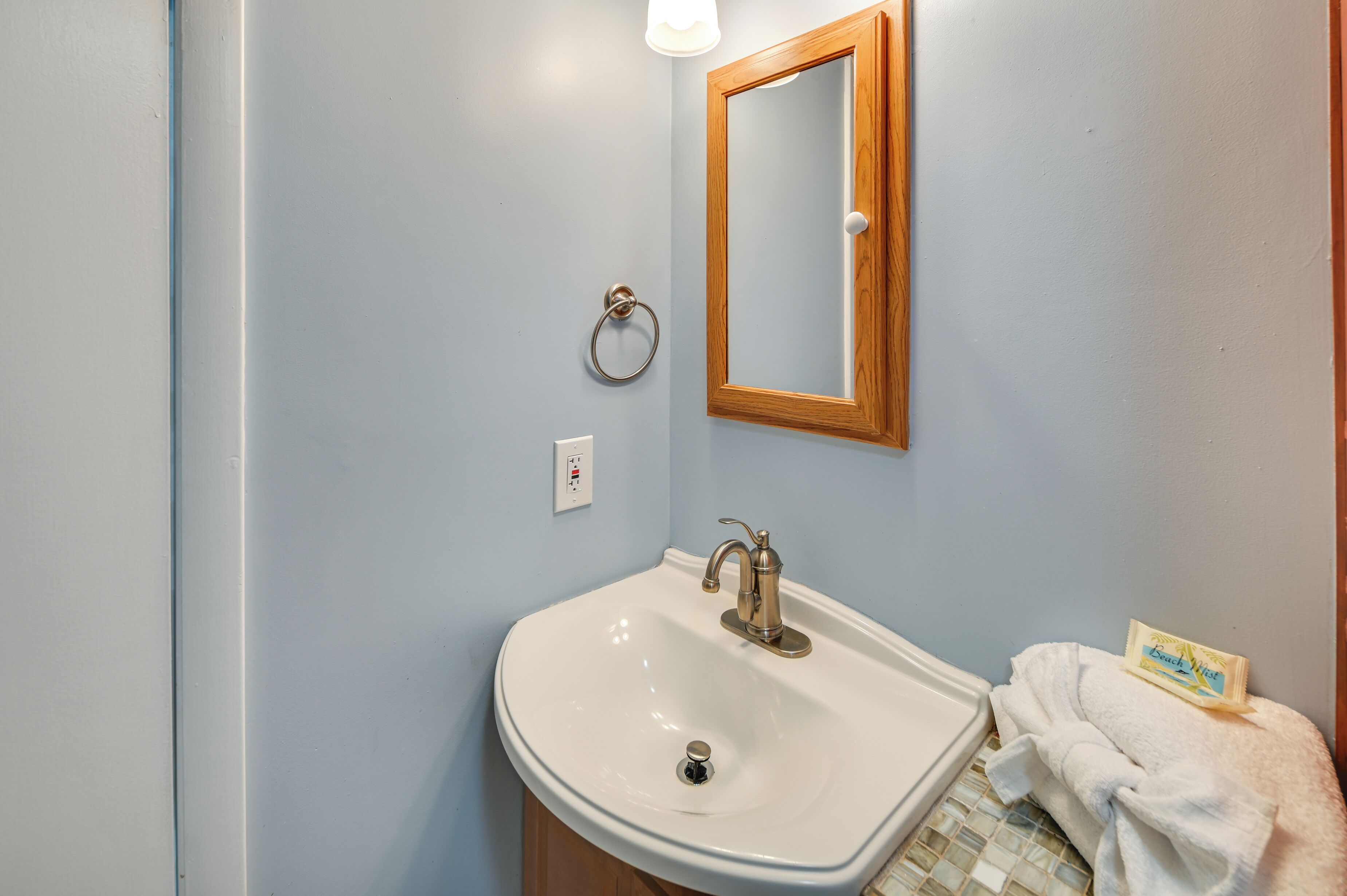 Une salle de bain avec un lavabo blanc, un miroir à cadre en bois, une serviette et un distributeur de savon.