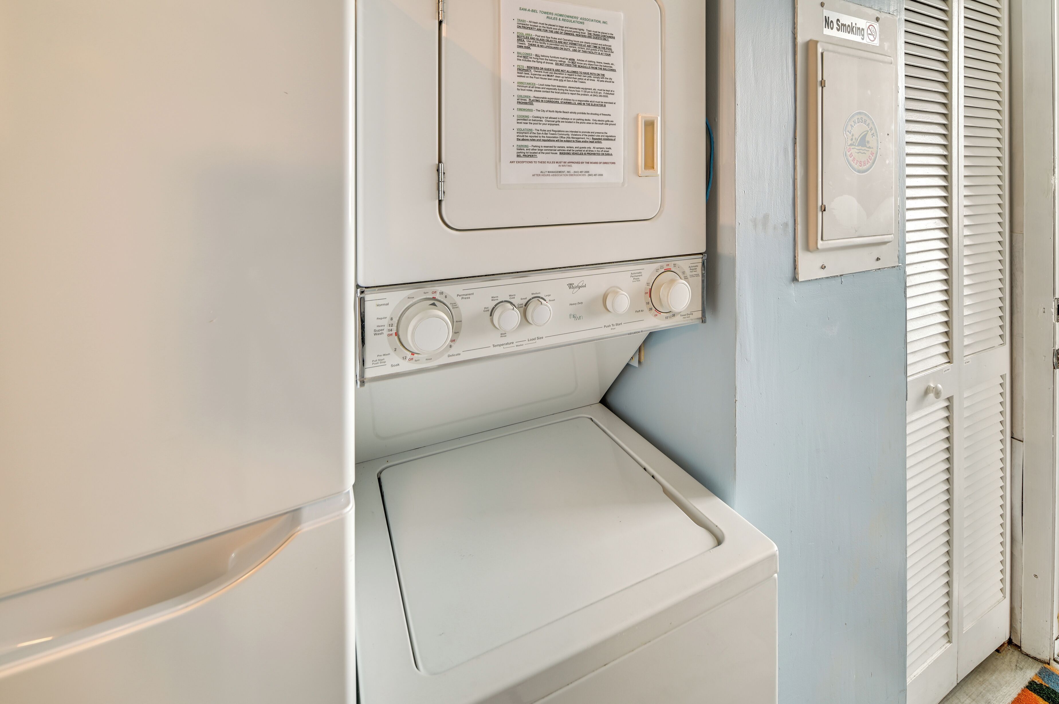 A laundry area with a white washer and dryer, a no-smoking sign, and a vent.