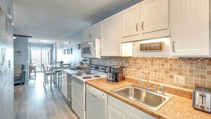 A modern kitchen with white cabinets, a granite countertop, stainless steel sink, and a coffee maker. - Coastal Condo w/ Balcony in North Myrtle Beach! (North Myrtle Beach)
